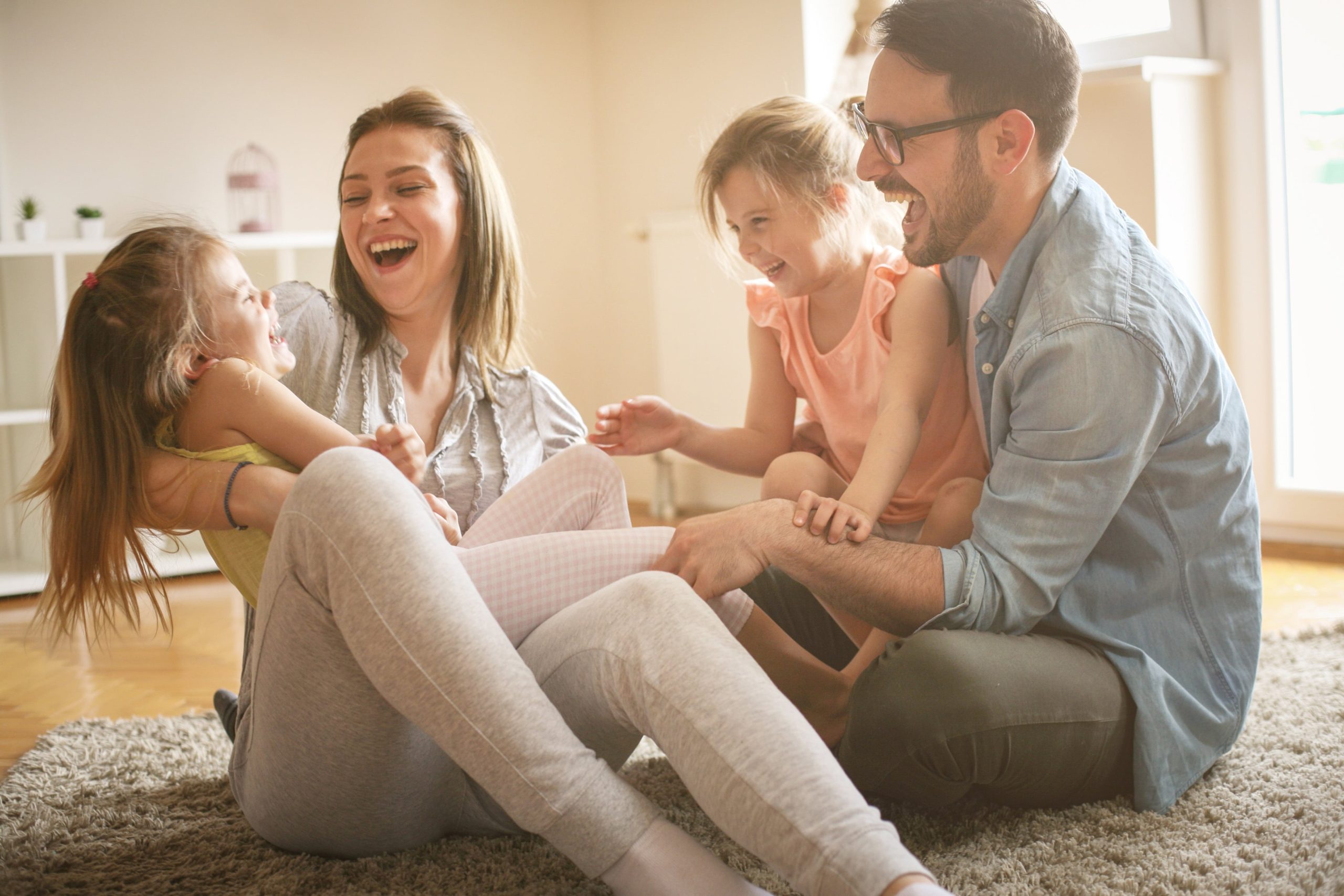 Happy Family With Two Daughters Playing At Home. Family Sitting On Floor And Playing Together